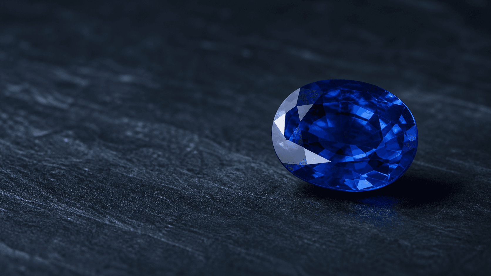 A deep blue natural Ceylon sapphire on a dark stone surface
